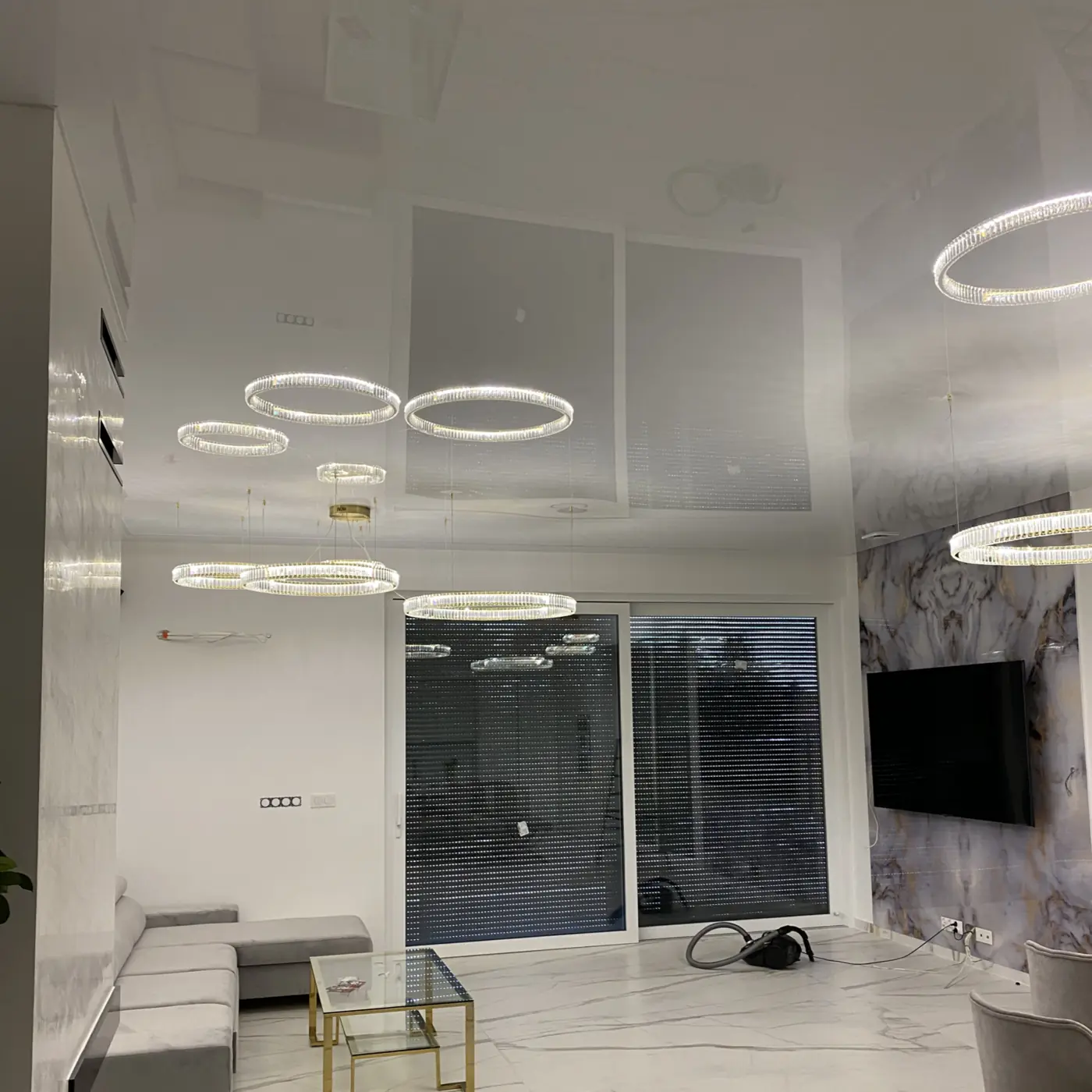 Biały połyskowy sufit napinany bez łączeń nad salonem z jadalnią, okrągłe lampy wiszące